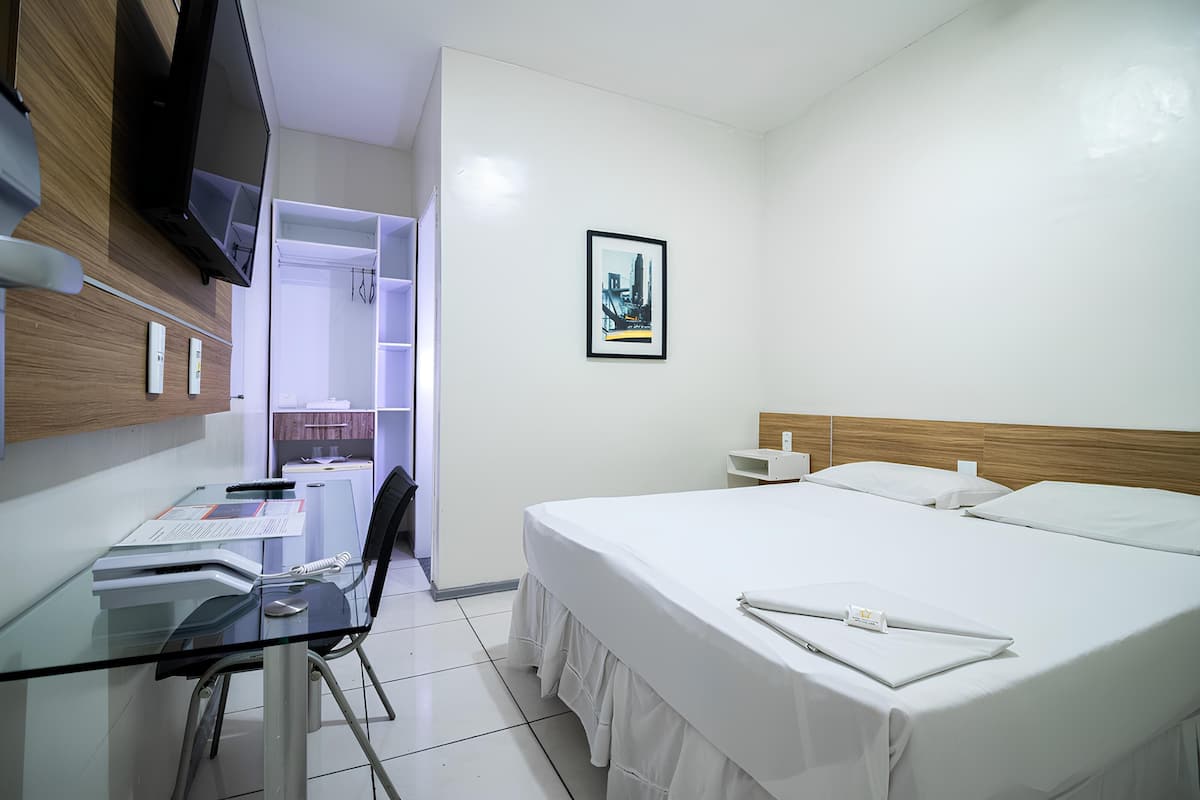 Een hotelkamer met een bed, een bureau met stoel, een televisie en een ingelijst schilderij aan de muur.