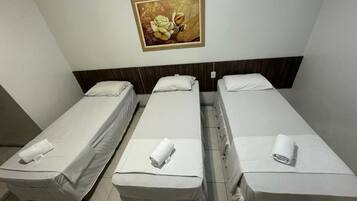 Una camera d'albergo con tre letti singoli, ognuno con copripiumino bianco e asciugamano arrotolato. Un quadro è appeso al muro sopra i letti.