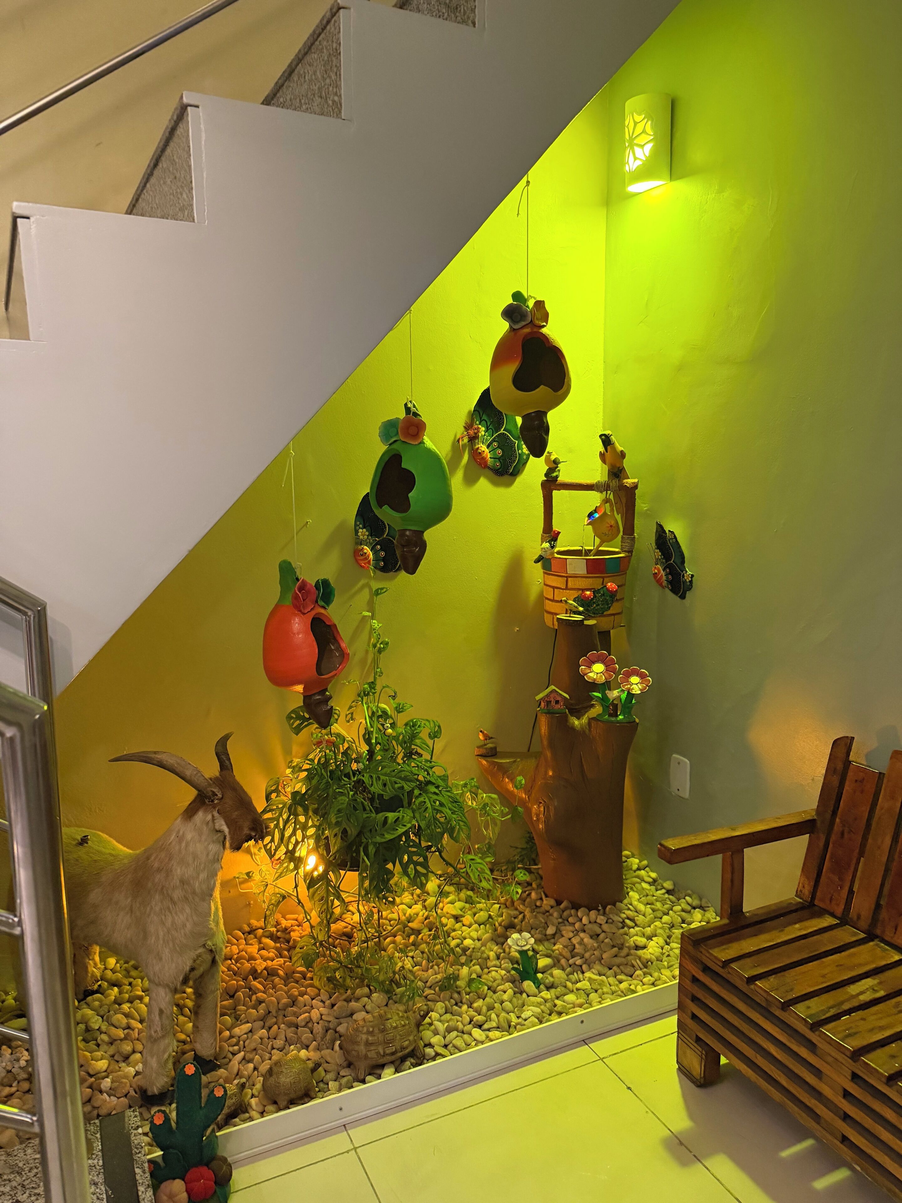 Una habitación con pared verde, un banco de madera, una mesa pequeña y un adorno colgante en la pared.