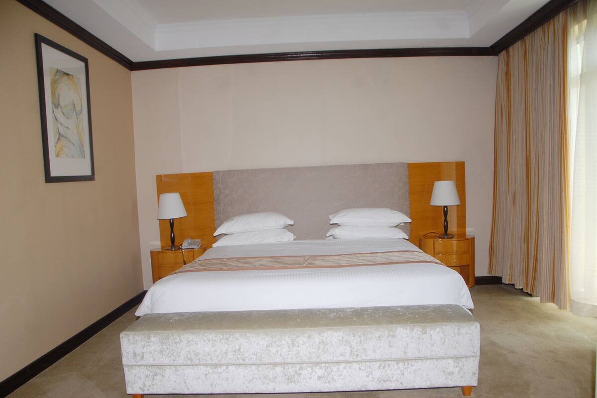 A neatly made bed with white linens, two bedside tables with lamps, and a large painting on the wall.