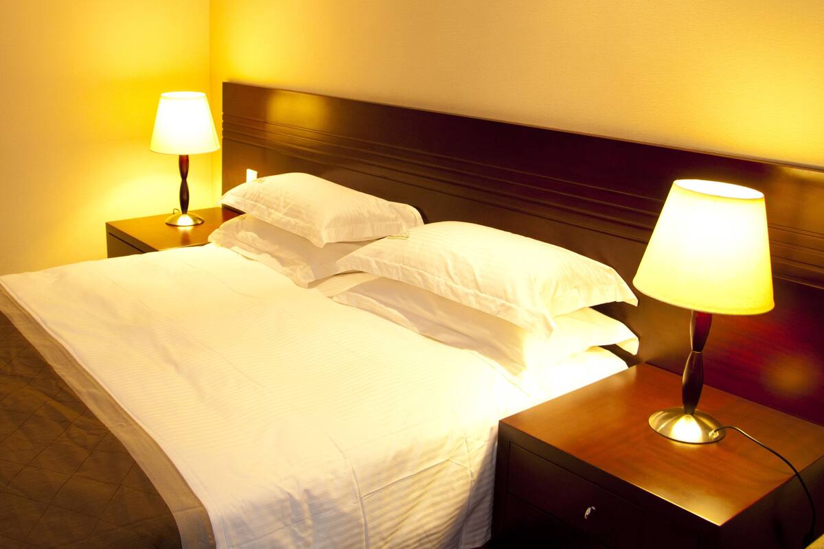 A neatly made bed with white linens, two bedside lamps, and a wooden headboard.
