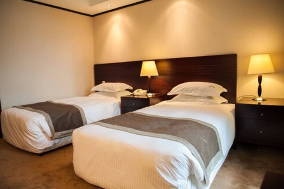 A hotel room with two beds, each with a nightstand and a lamp.