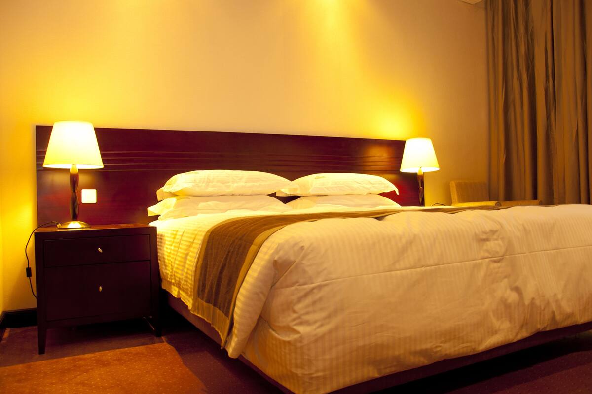 A hotel room with a large bed, two bedside lamps, a nightstand, and a window with curtains.