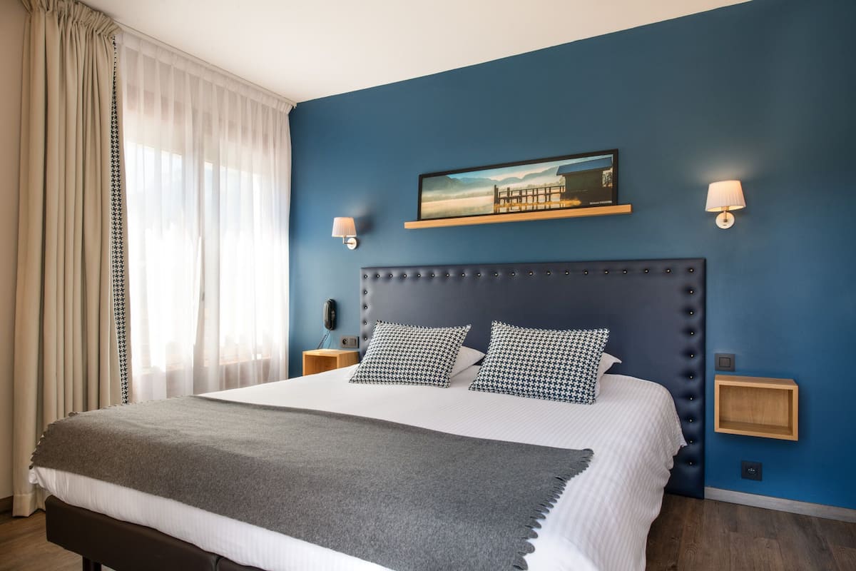 Un dormitorio con una cama grande, dos mesitas de noche, un cabecero, un cuadro en la pared y una ventana con cortinas.