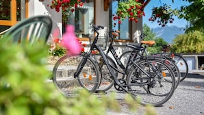 Una bicicleta estacionada bajo una pérgola de madera con flores rojas colgantes.