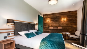 Una habitación de hotel moderna con una cama grande, un panel de madera decorativo, una pequeña mesa con una silla y una lámpara fijada a la pared.