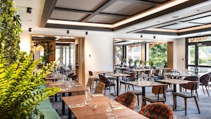 Un restaurante con varias mesas y sillas, ventanas amplias y plantas de interior.