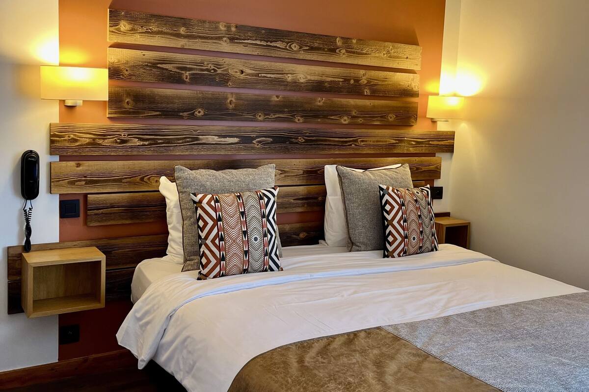 Un dormitorio con cabecera de madera, dos lámparas de noche, un teléfono junto a la cama y almohadas estampadas.
