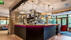 Un área de bar moderna con una barra curva, iluminación colgante y vistas a espacios verdes al exterior.