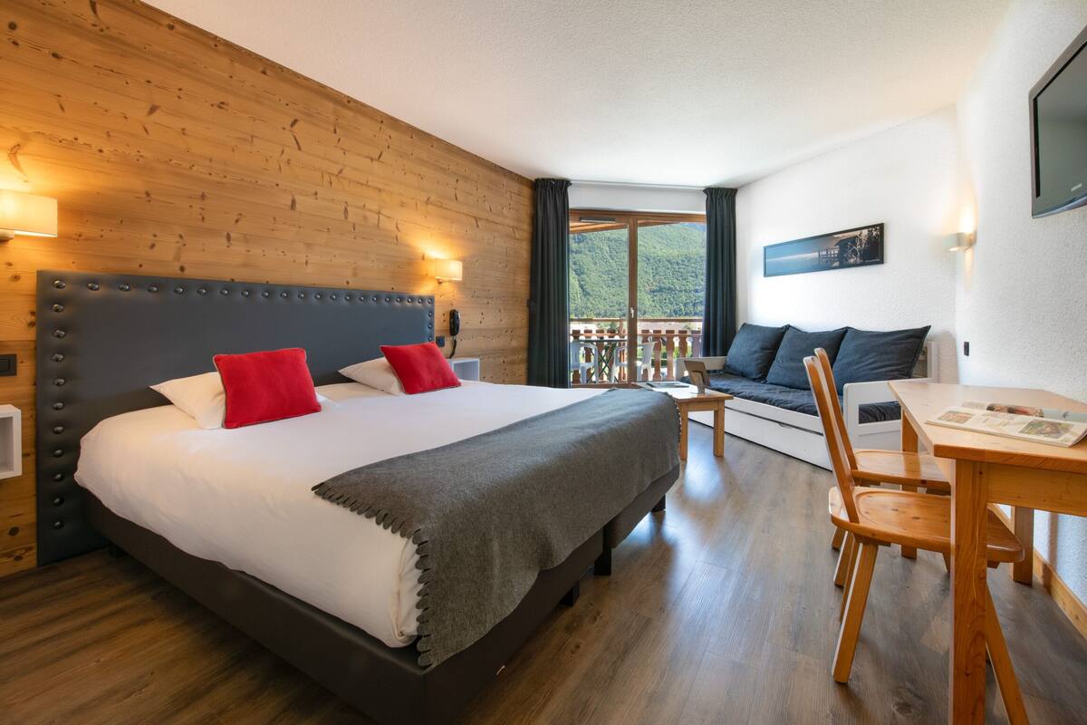 Un dormitorio con una cama grande, cabecera de madera, un balcón con vistas y un comedor con mesa y sillas.