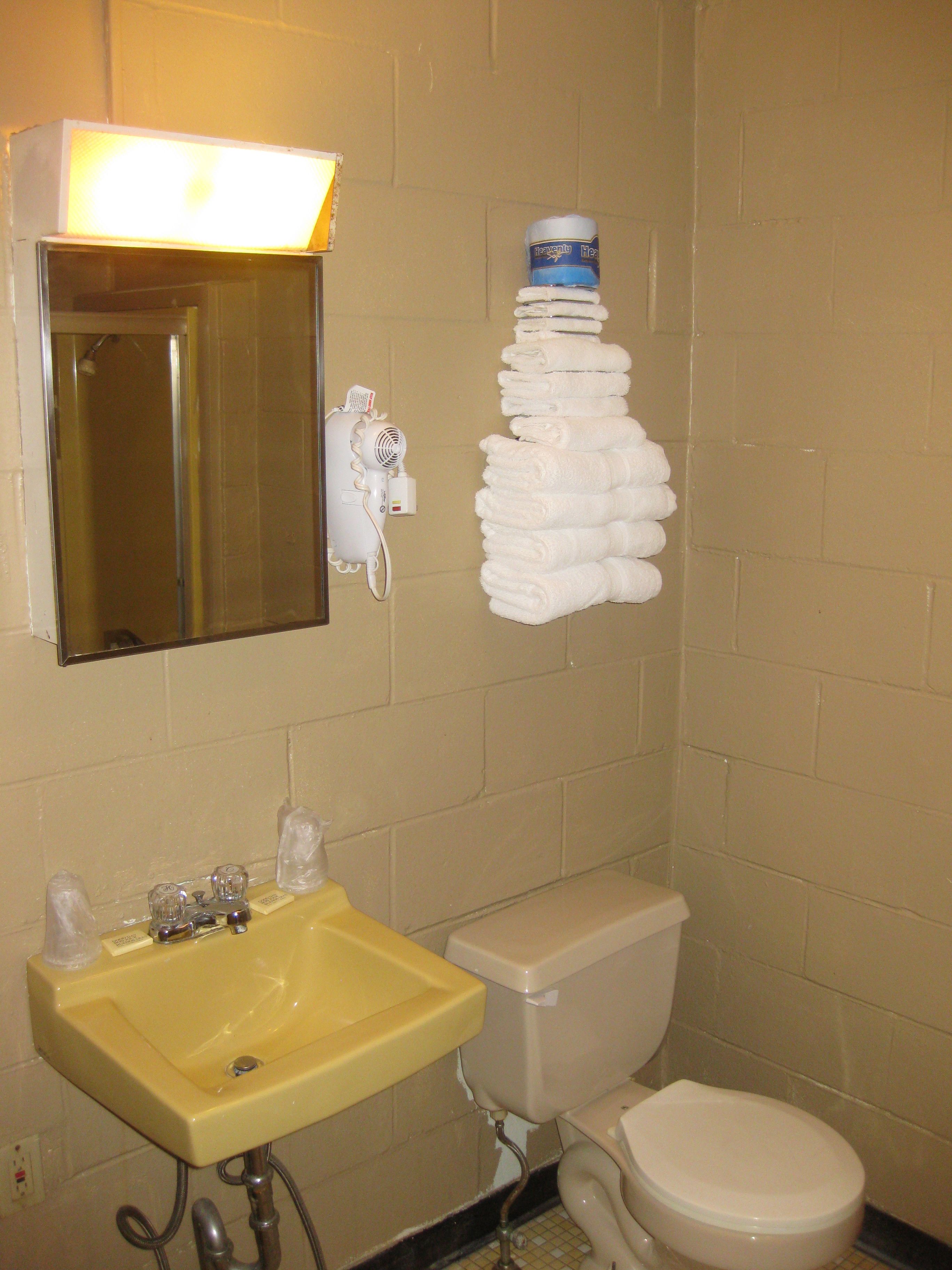 A bathroom with a yellow sink, a white toilet, a mirror, and a stack of white towels on the wall.