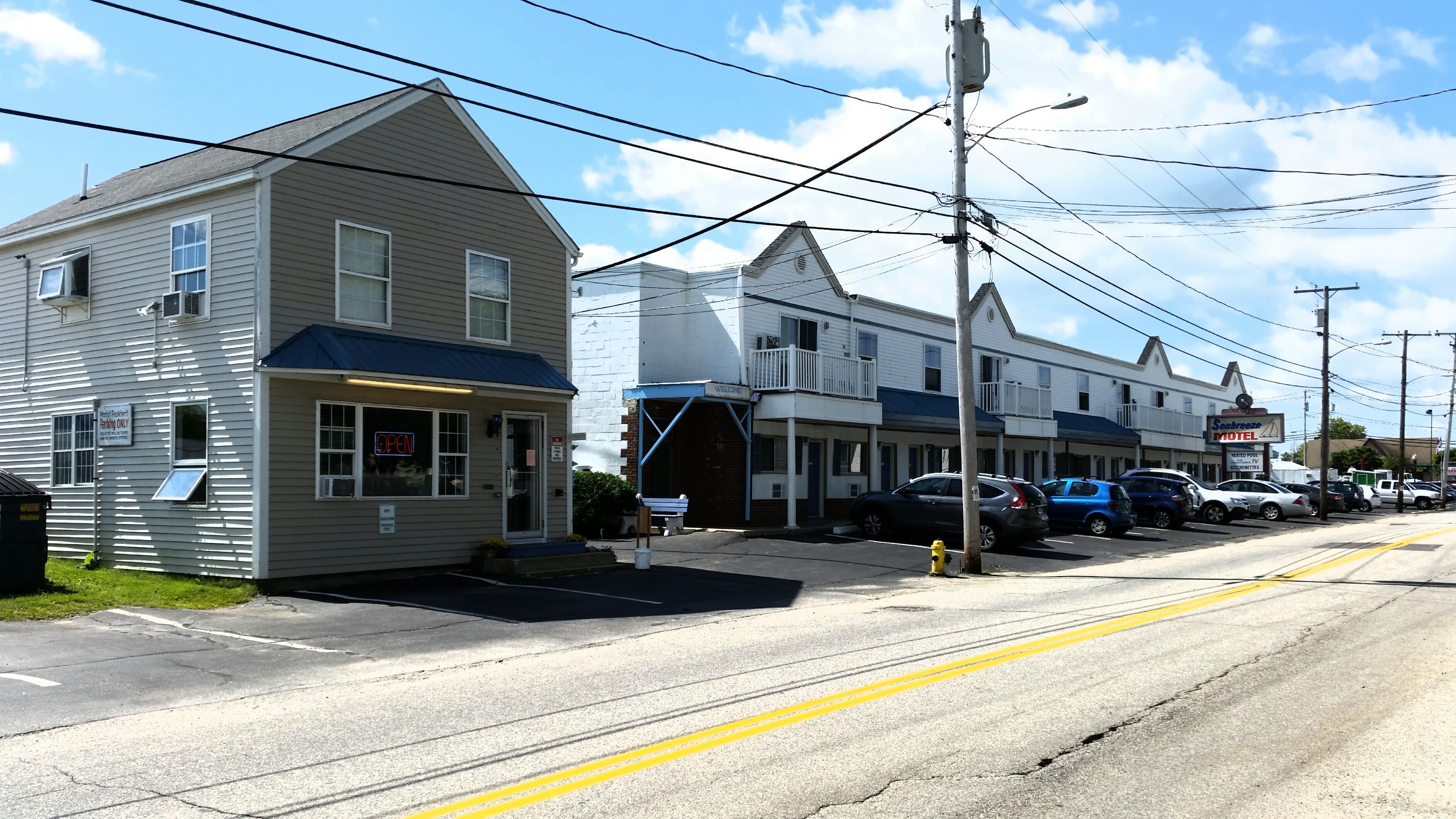 A motel with a 'Welcome' sign, a parking lot, and several parked cars.