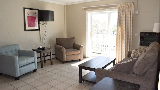 A living room with a sofa, armchair, and a television mounted on the wall. - Seabreeze Motel (Old Orchard Beach)