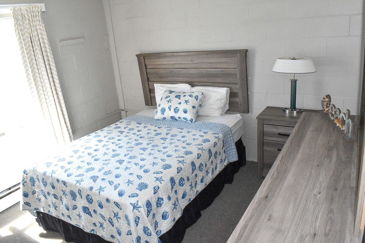 A hotel room with a bed, a nightstand, a lamp, and a wooden bench.