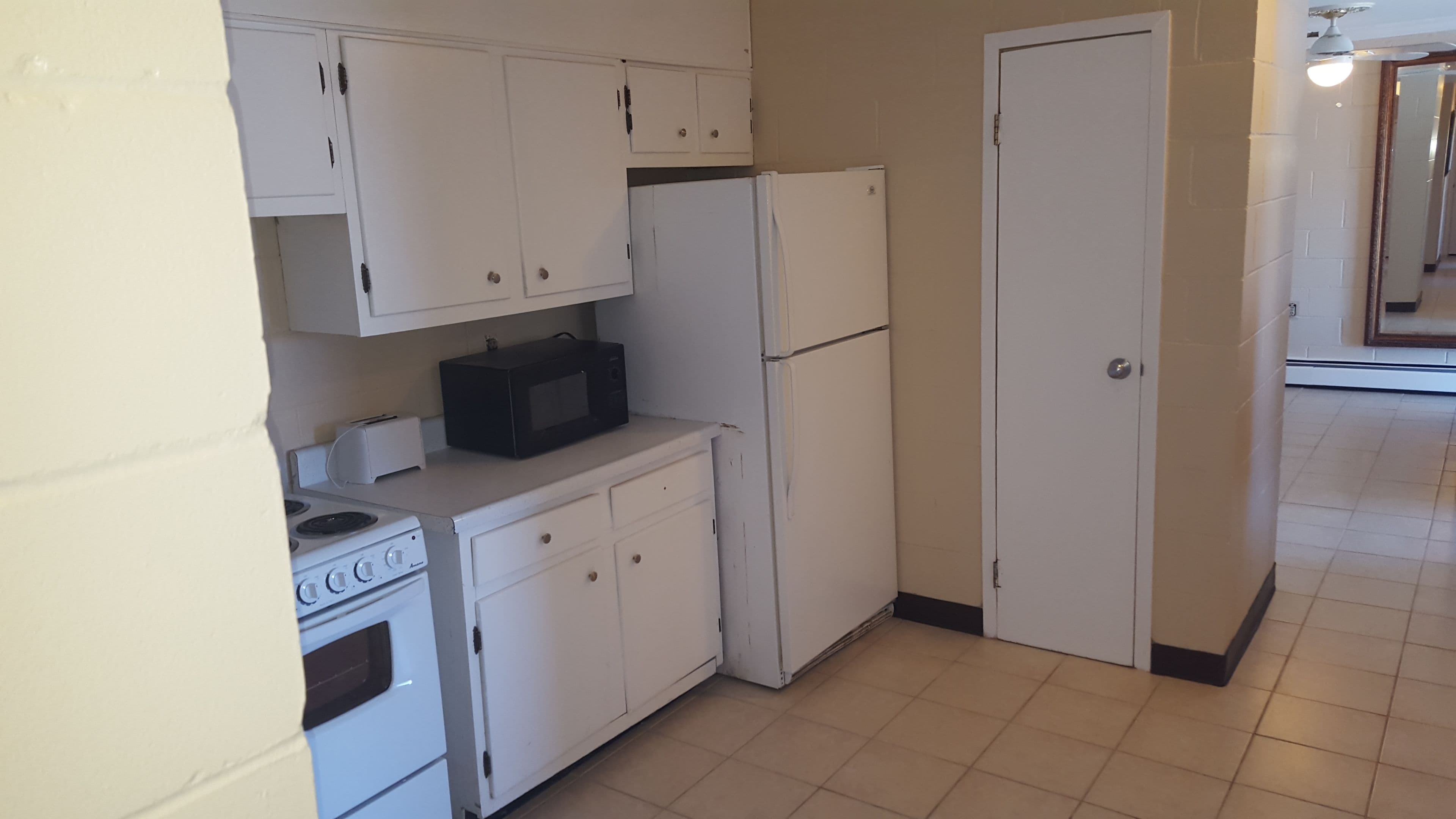 A compact kitchen with white cabinets, a microwave, a refrigerator, and a stove.