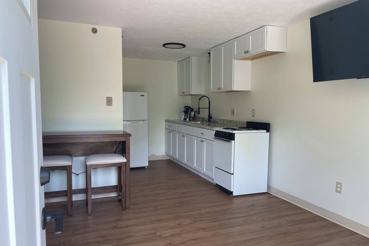 A compact kitchen with white cabinets, a built-in oven, and a small dining area with two chairs.