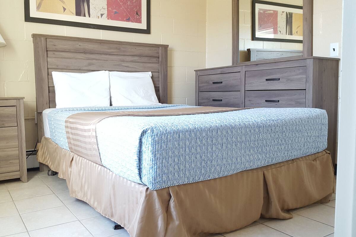 A bedroom with a bed, a nightstand, a dresser, and a lamp.