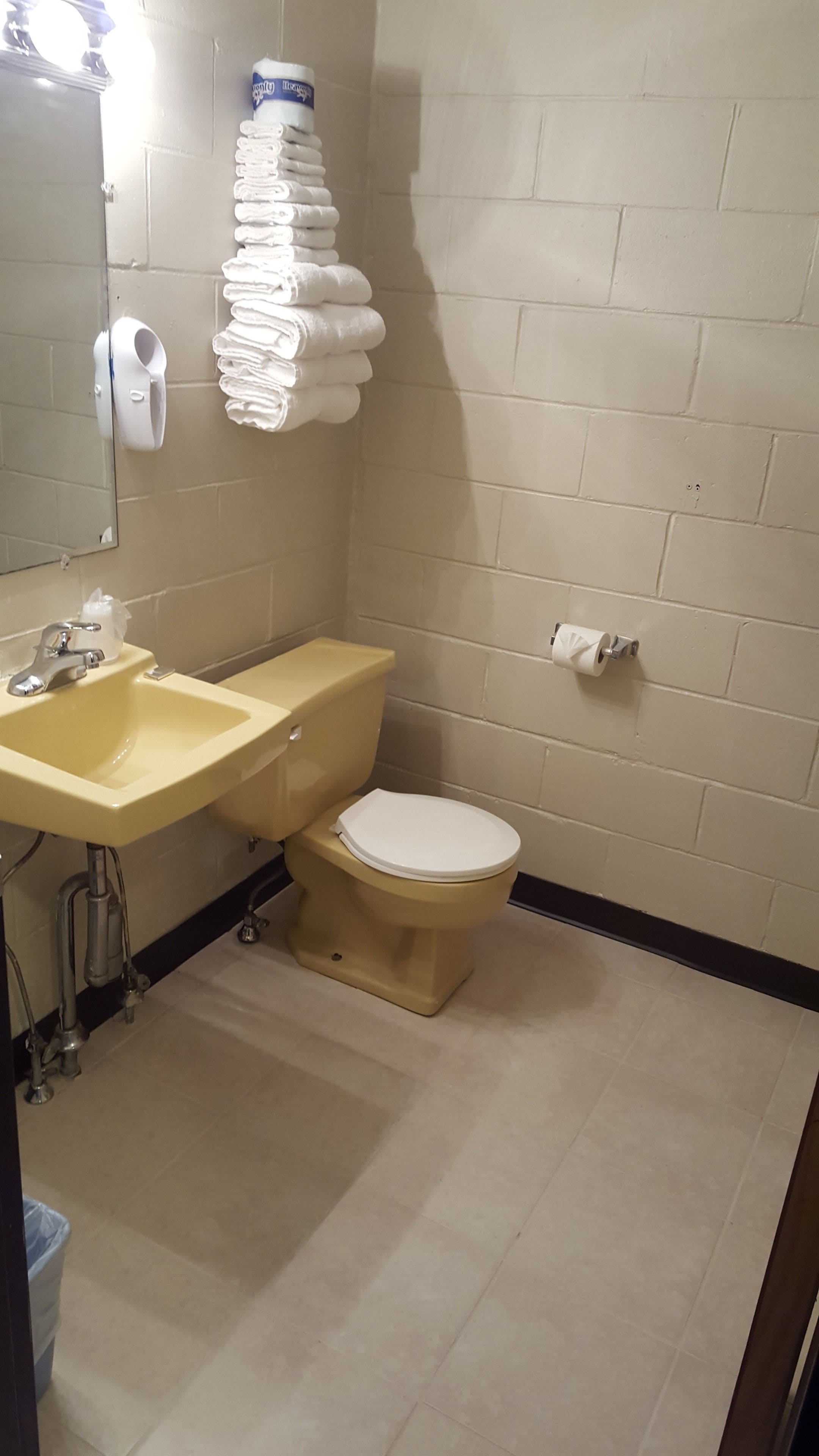 A small bathroom with a sink, toilet, and a stack of white towels.