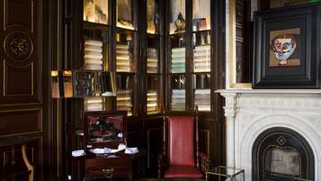 A library with bookshelves, a red leather chair, a fireplace, and a clock.