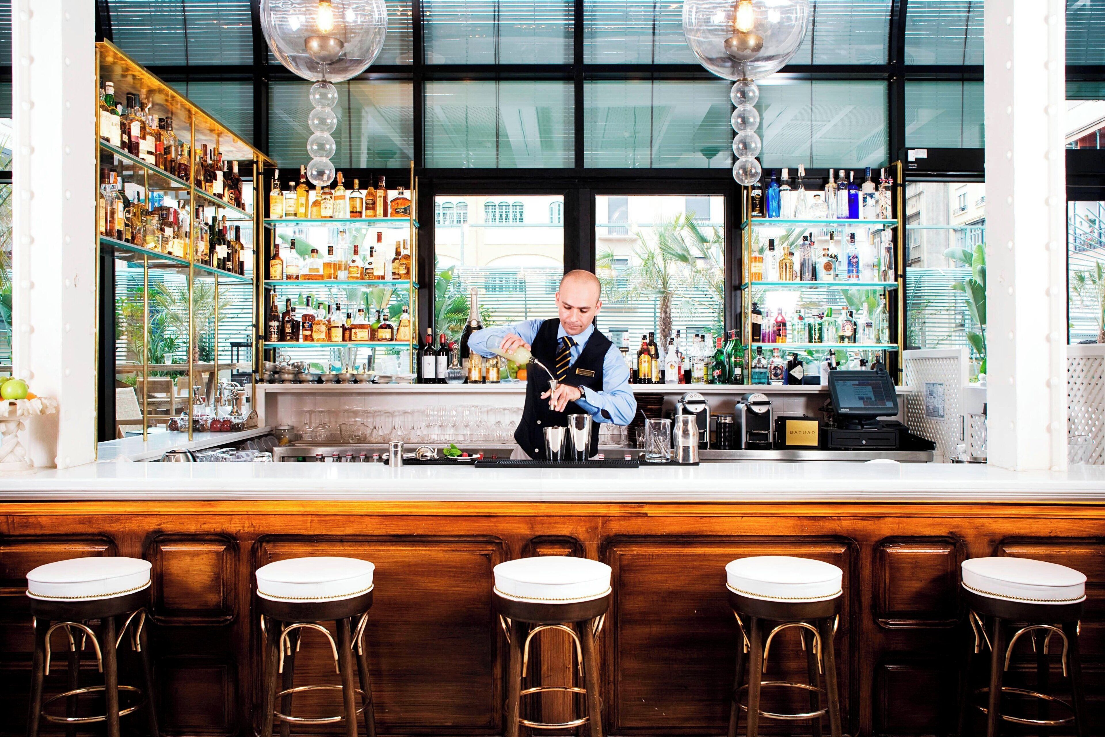 A bar with a bartender preparing drinks, shelves of liquor, and bar stools.