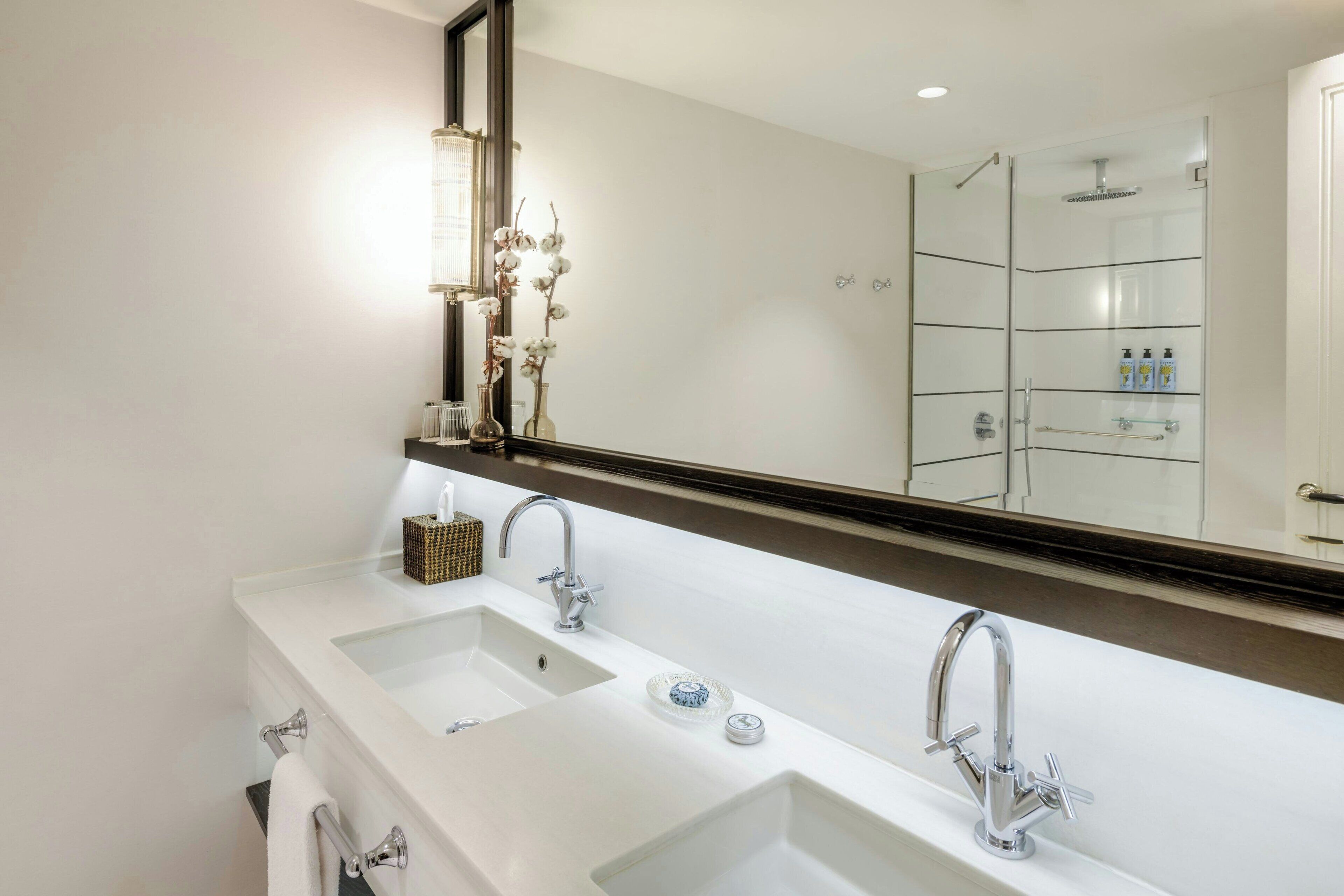 A modern bathroom with two sinks, a large mirror, and a glass-enclosed shower.