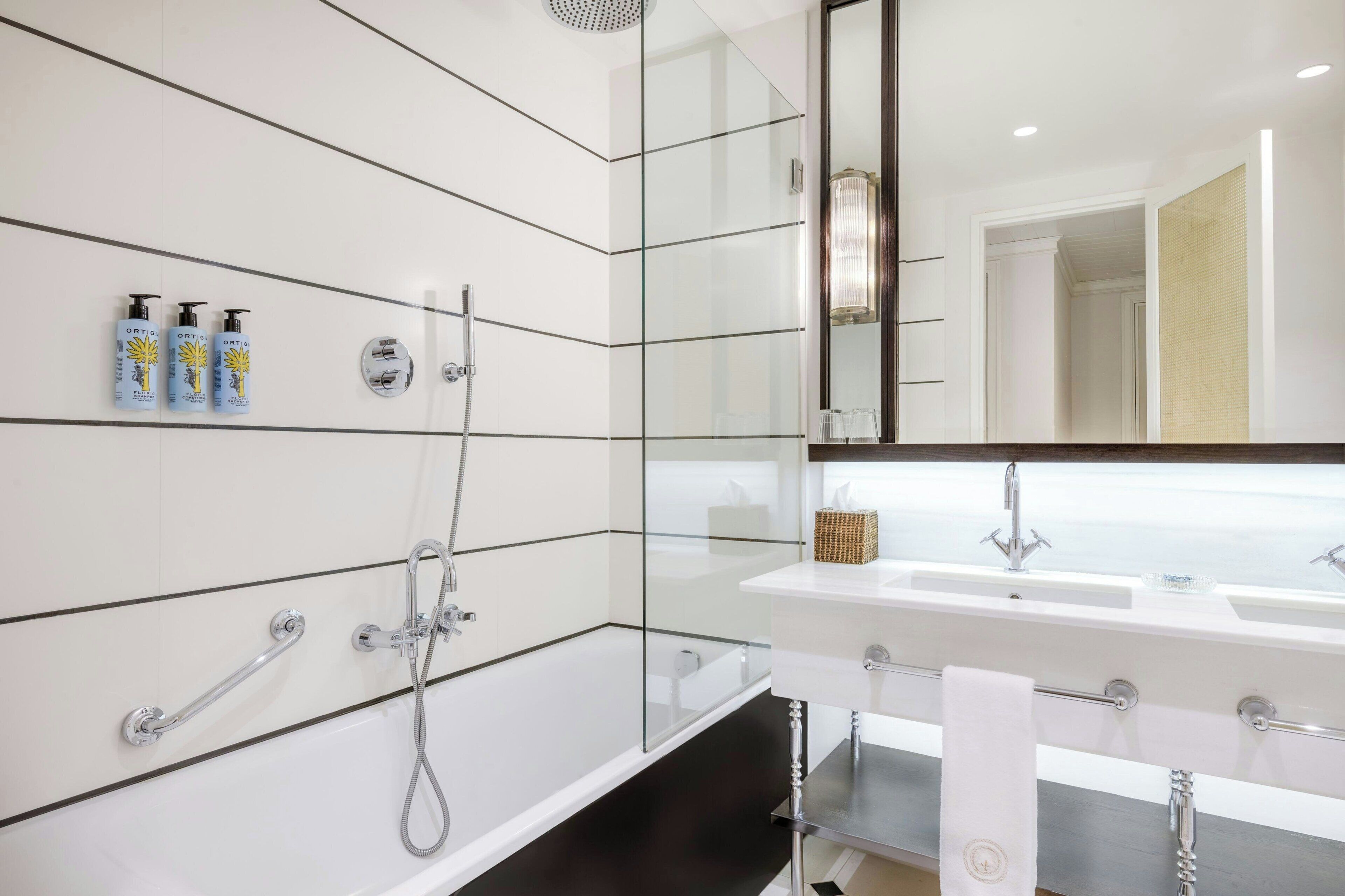 A modern bathroom with a glass shower enclosure, a white bathtub, and a large mirror.