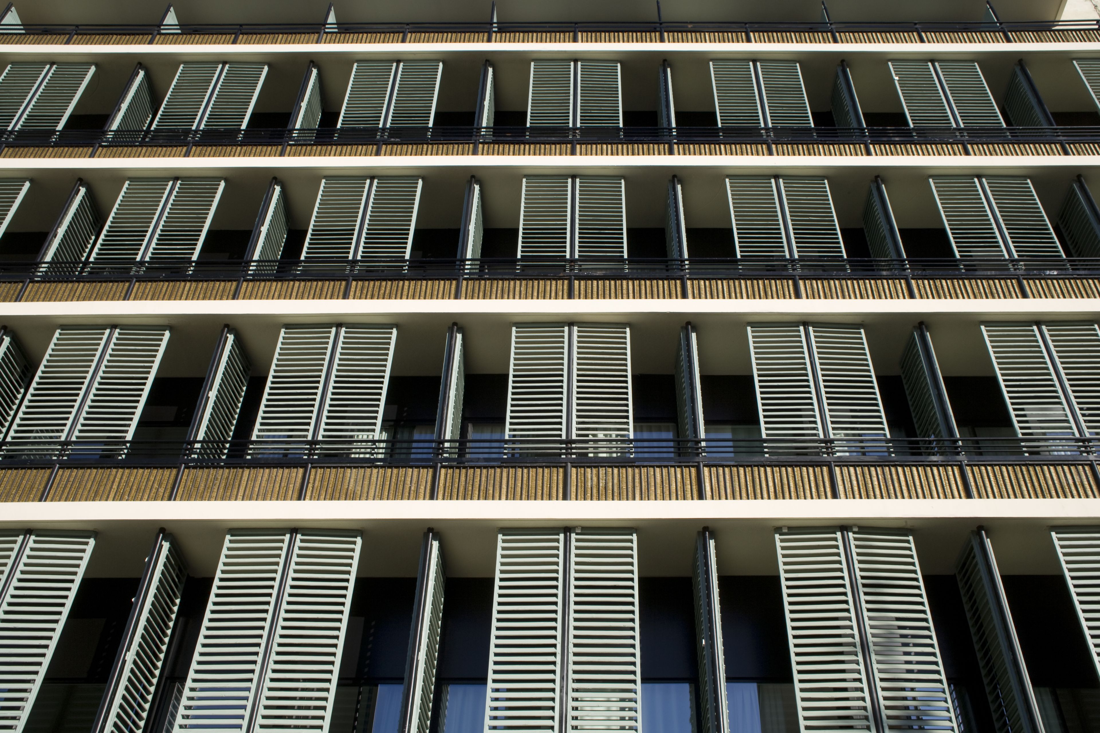 Un edificio de varios pisos con fachada uniforme, que presenta balcones regularmente espaciados y barandillas de metal.