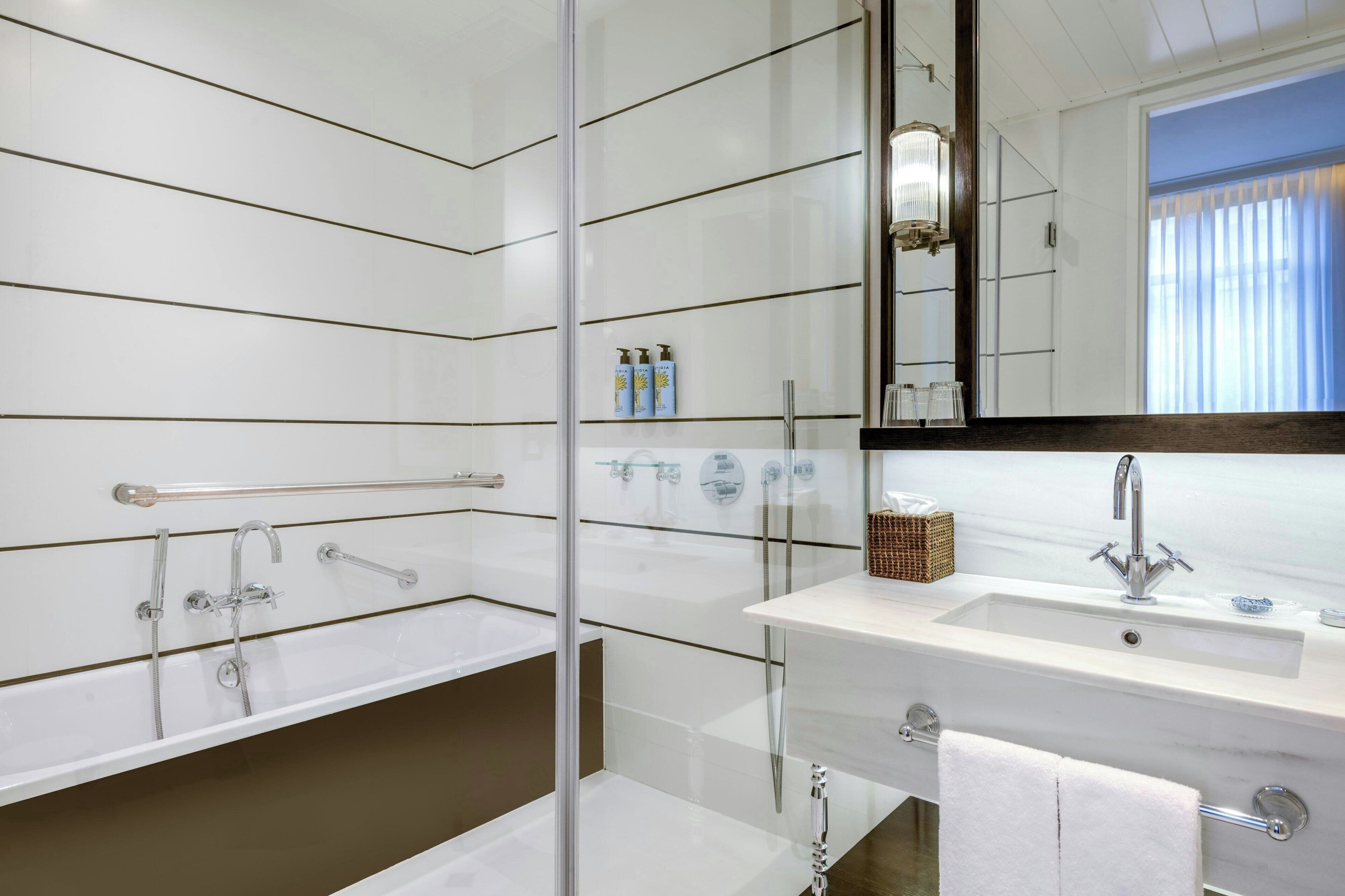 Un baño moderno con ducha envuelta en vidrio, un lavabo blanco con un espejo encima y un perchero para toallas.
