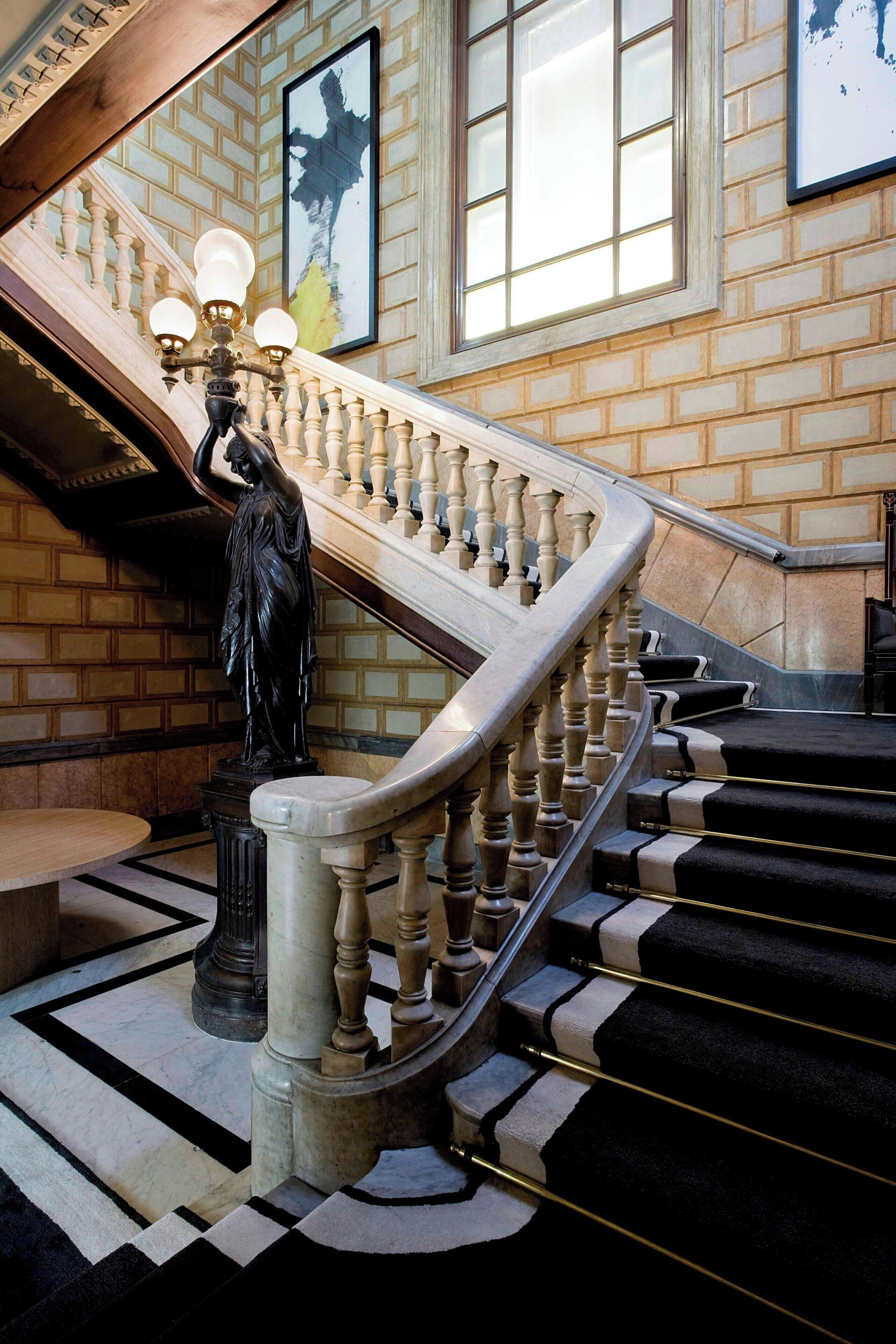 Una gran escalera con barandilla, una estatua y un candelabro.