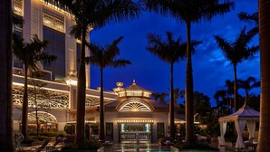 Un hotel lujoso con una piscina grande, palmeras y una entrada bien iluminada.