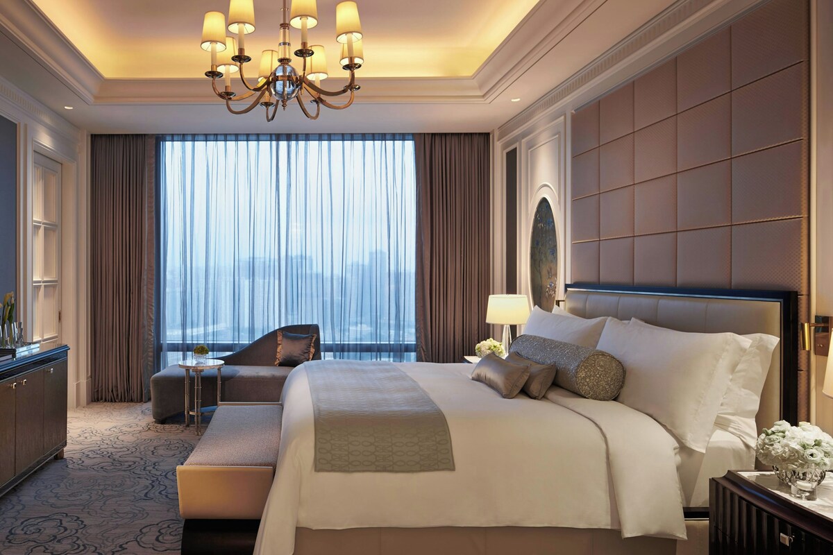 Habitación de hotel con una cama grande, un rincón de descanso, un escritorio y vistas a la ciudad desde la ventana.