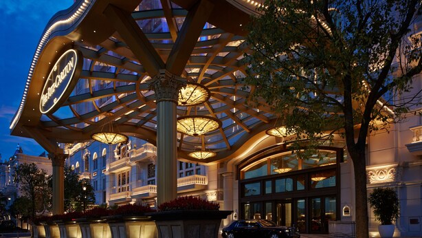 Majestuosa entrada de hotel con un amplio toldo iluminado y columnas, rodeada de exuberante vegetación y un estilo arquitectónico clásico.