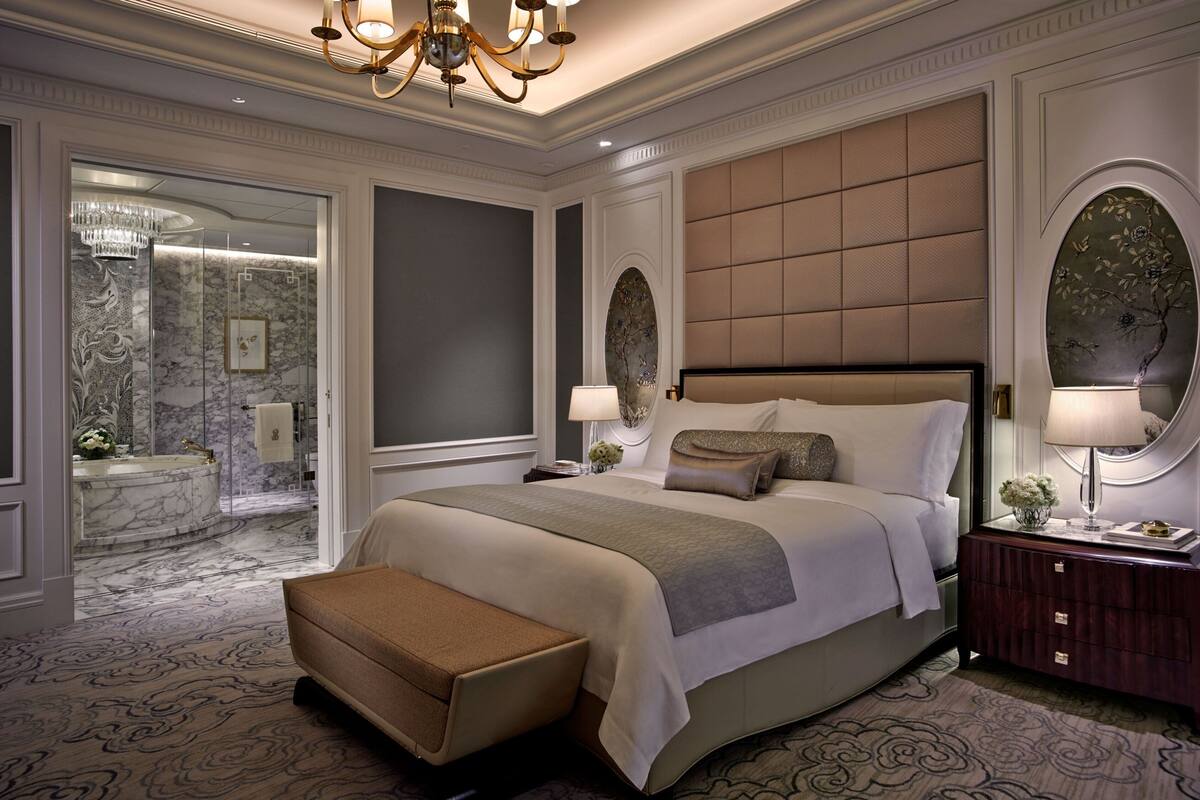 A spacious bedroom with a large bed, a bench, a nightstand, and a mirror.