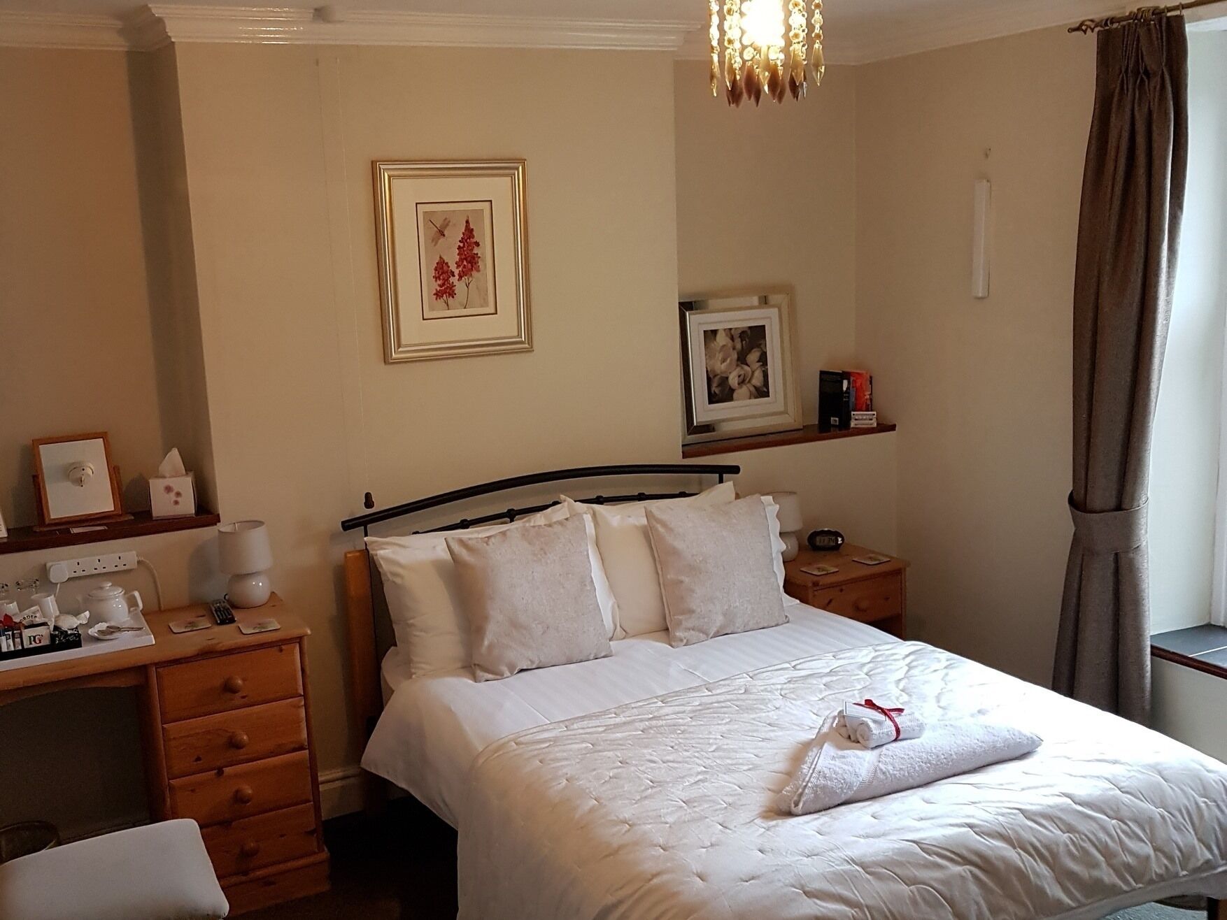Une chambre d’hôtel comprenant un lit, une table de chevet, un bureau et une petite étagère avec des photos encadrées.