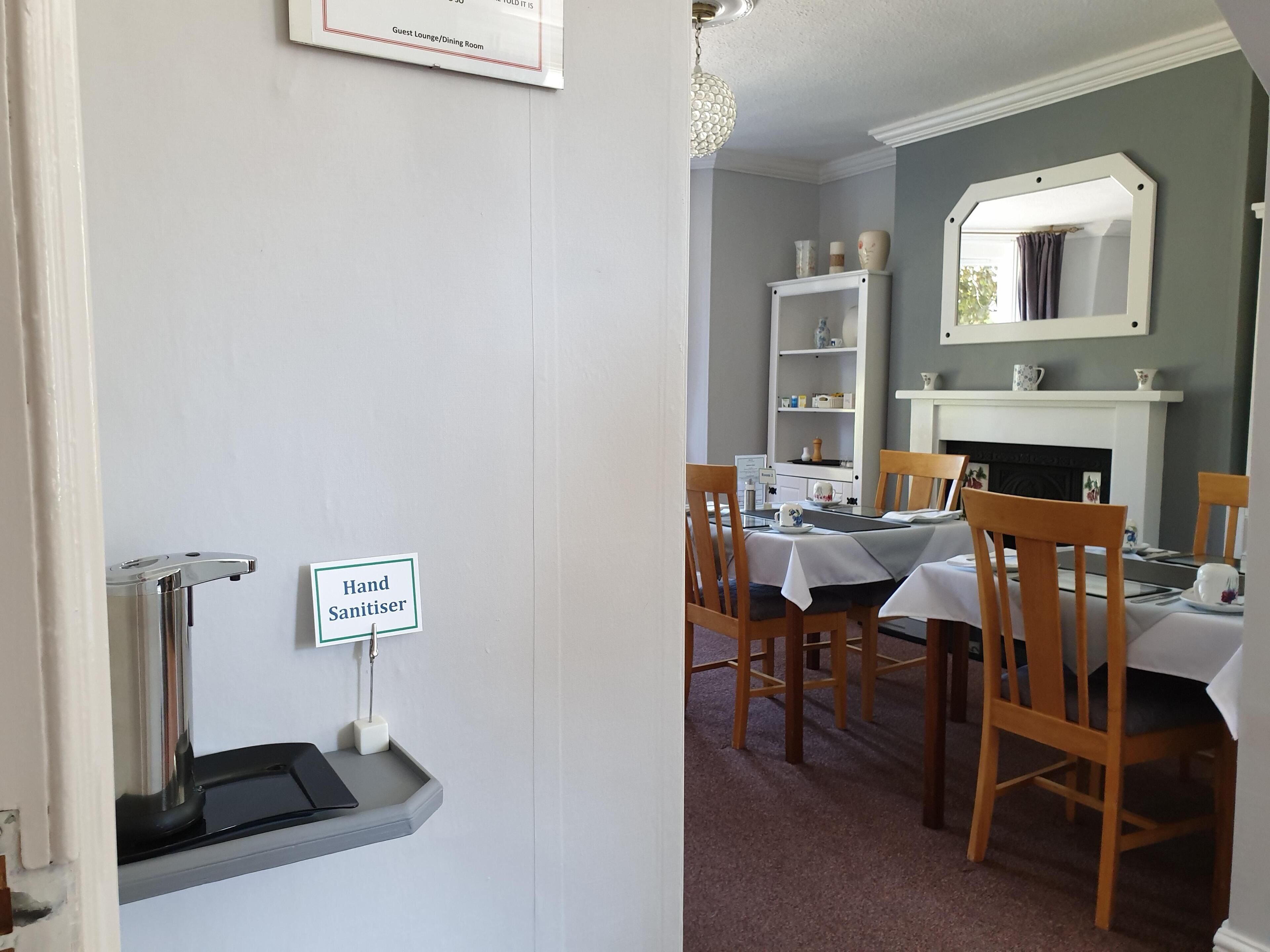 A dining area with a hand sanitizer dispenser, a fireplace, and a mirror above the mantel.