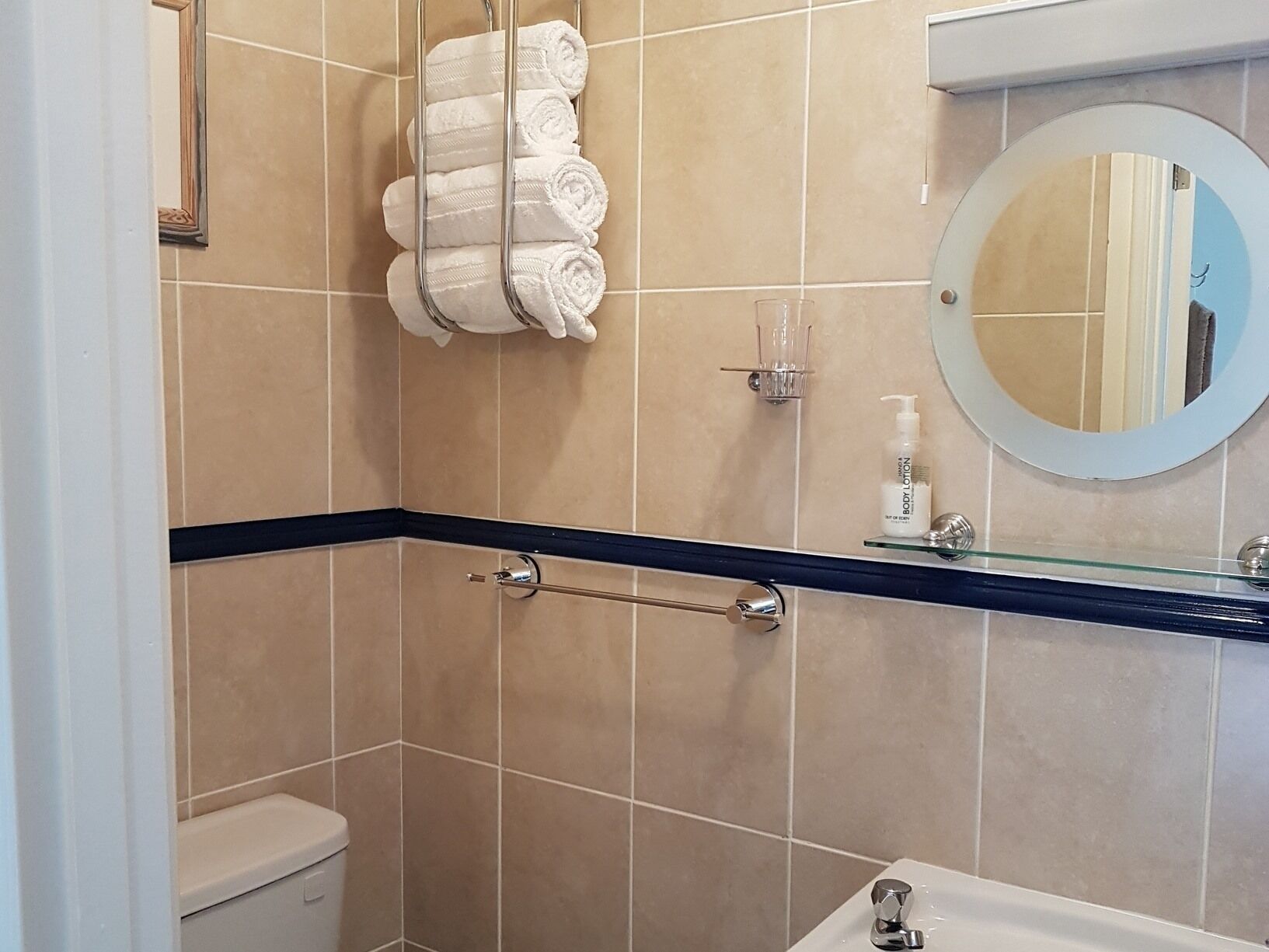 A bathroom with beige tiles, a black countertop, a glass shower enclosure, a toilet, and a sink with a mirror.