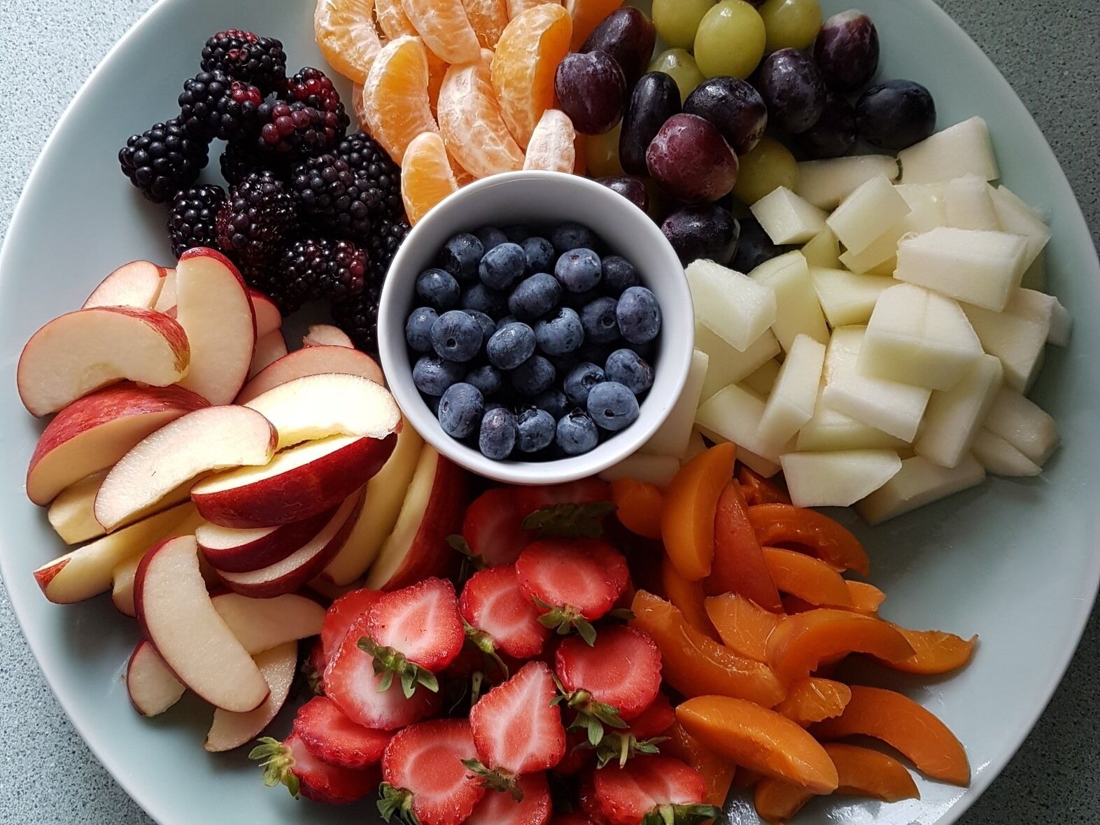 Une assiette de fruits variés, notamment des pommes, des fraises, des oranges, des raisins, des mûres et des myrtilles.