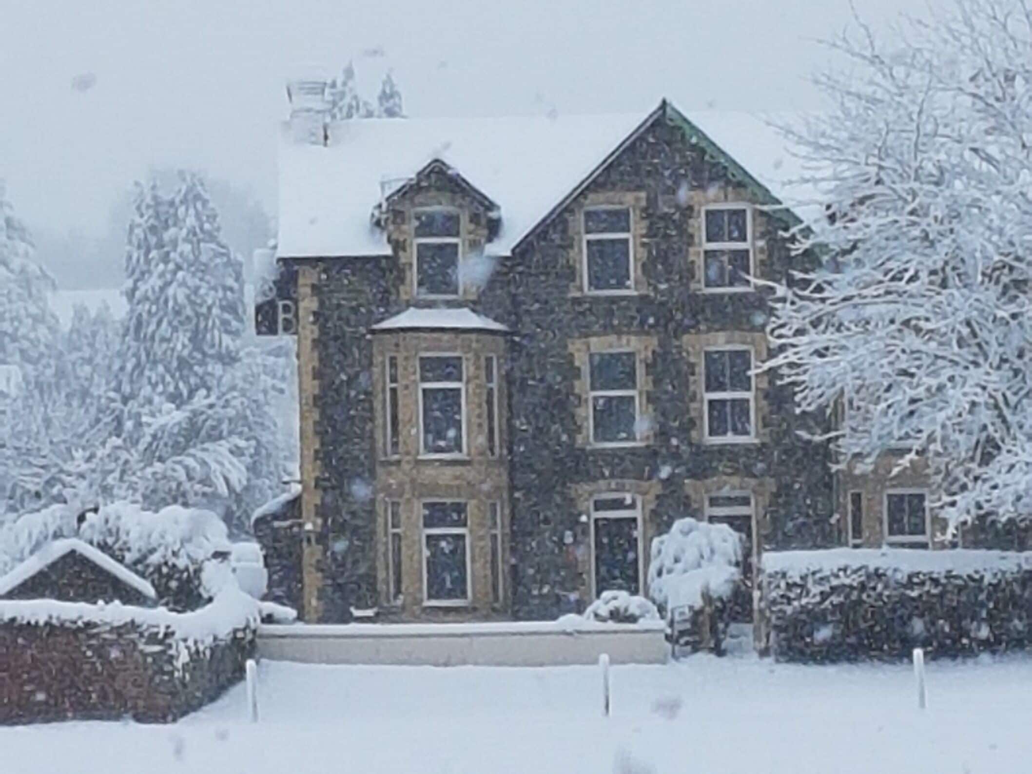 A multi-story stone building with a symmetrical facade, large windows, and a snow-covered roof.