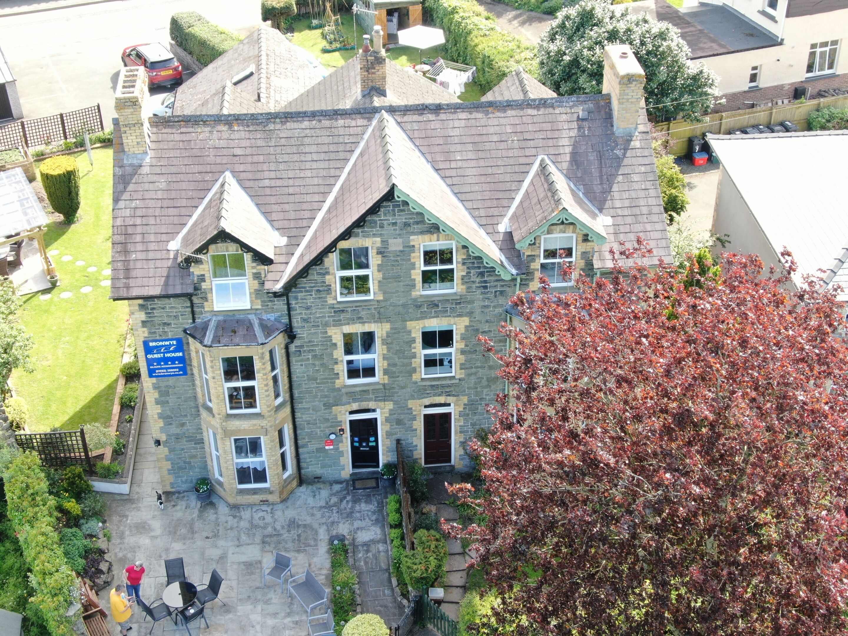 Un bâtiment en pierre doté d’une tourelle d’angle, une enseigne indiquant qu’il s’agit d’une maison d’hôtes, et une cour pavée avec des espaces aménagés pour s’asseoir à l’extérieur.