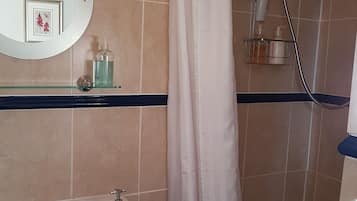 Une salle de bain avec une baignoire, une douche et un lavabo. On y trouve une étagère en verre où sont posés des articles de toilette, et un tableau encadré au-dessus du miroir.