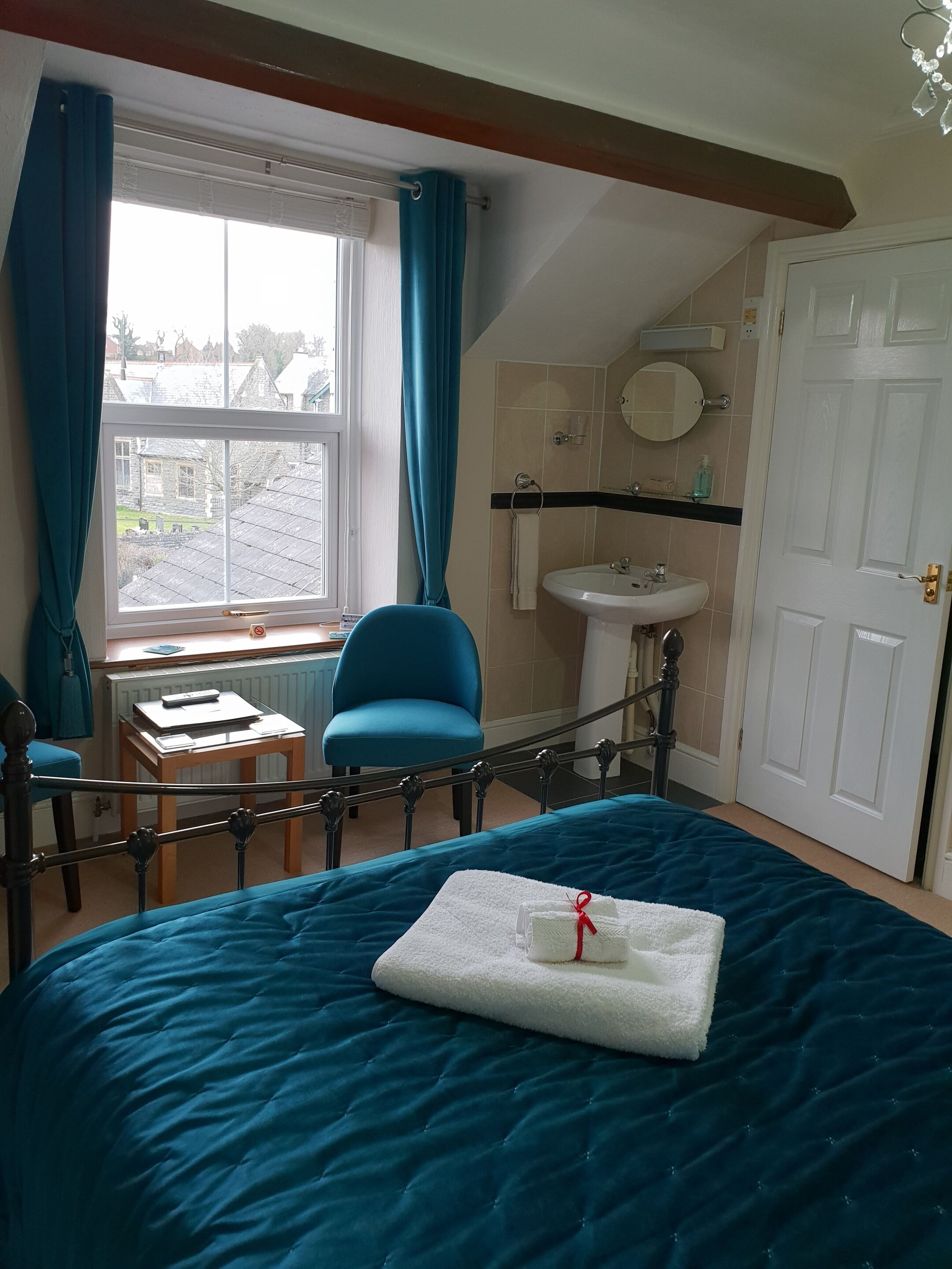 Une chambre à coucher comprenant un lit, une chaise, une petite table, une fenêtre avec des rideaux, un lavabo et une porte.