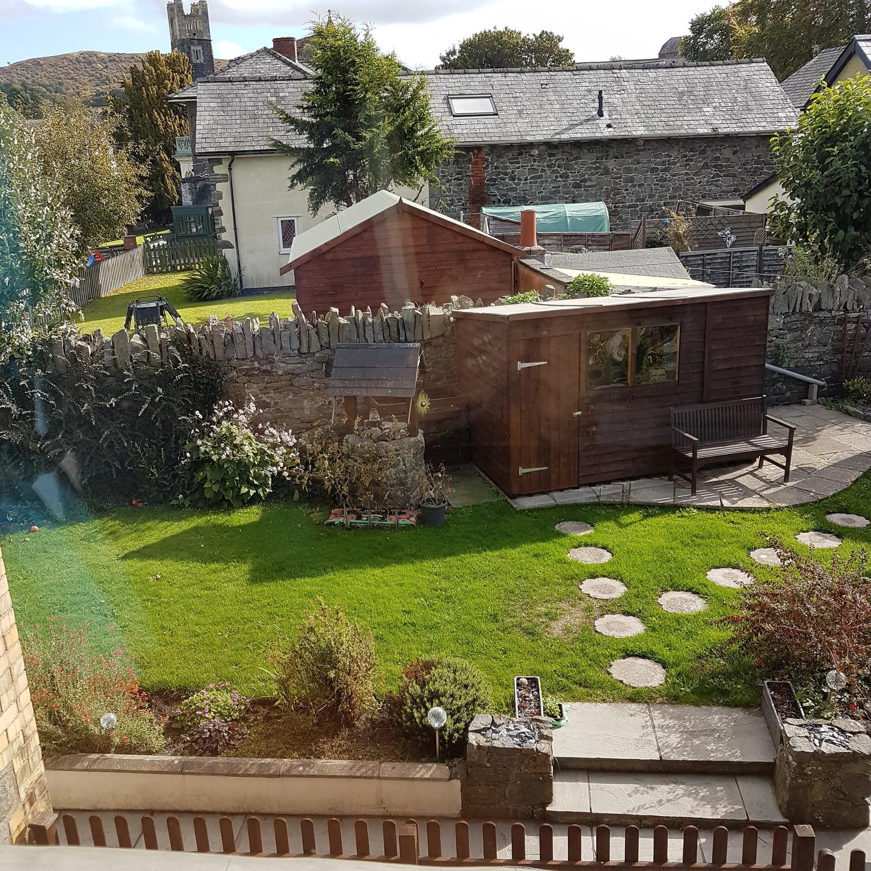 A garden with a wooden shed, a stone wall, and a lawn with stepping stones.