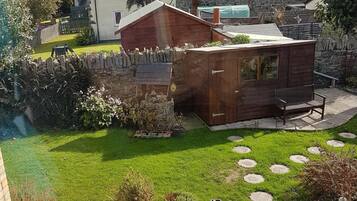 A garden with a wooden shed, a stone wall, and a lawn with stepping stones.