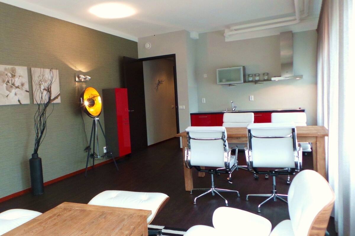 A modern hotel room with a dining area, a kitchen, and a hallway.