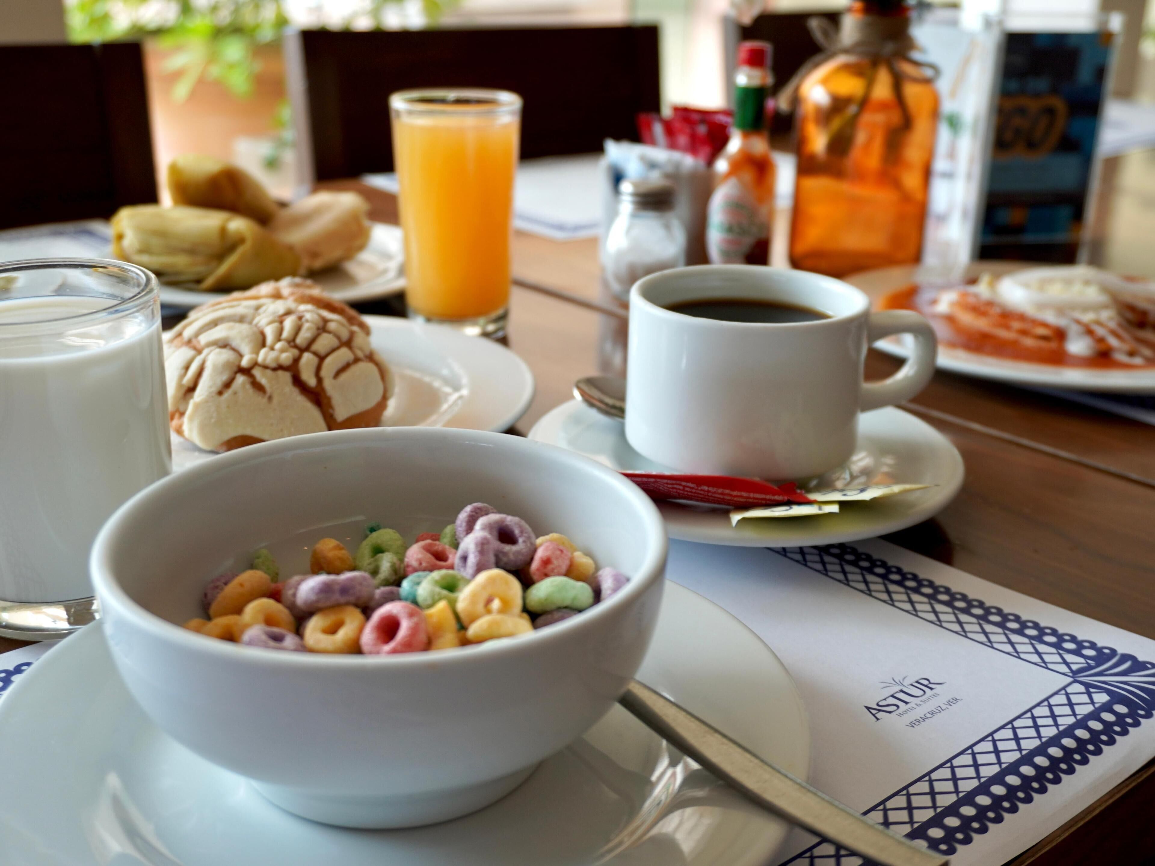 A breakfast table with a bowl of cereal, a glass of orange juice, a cup of coffee, and a plate of food.