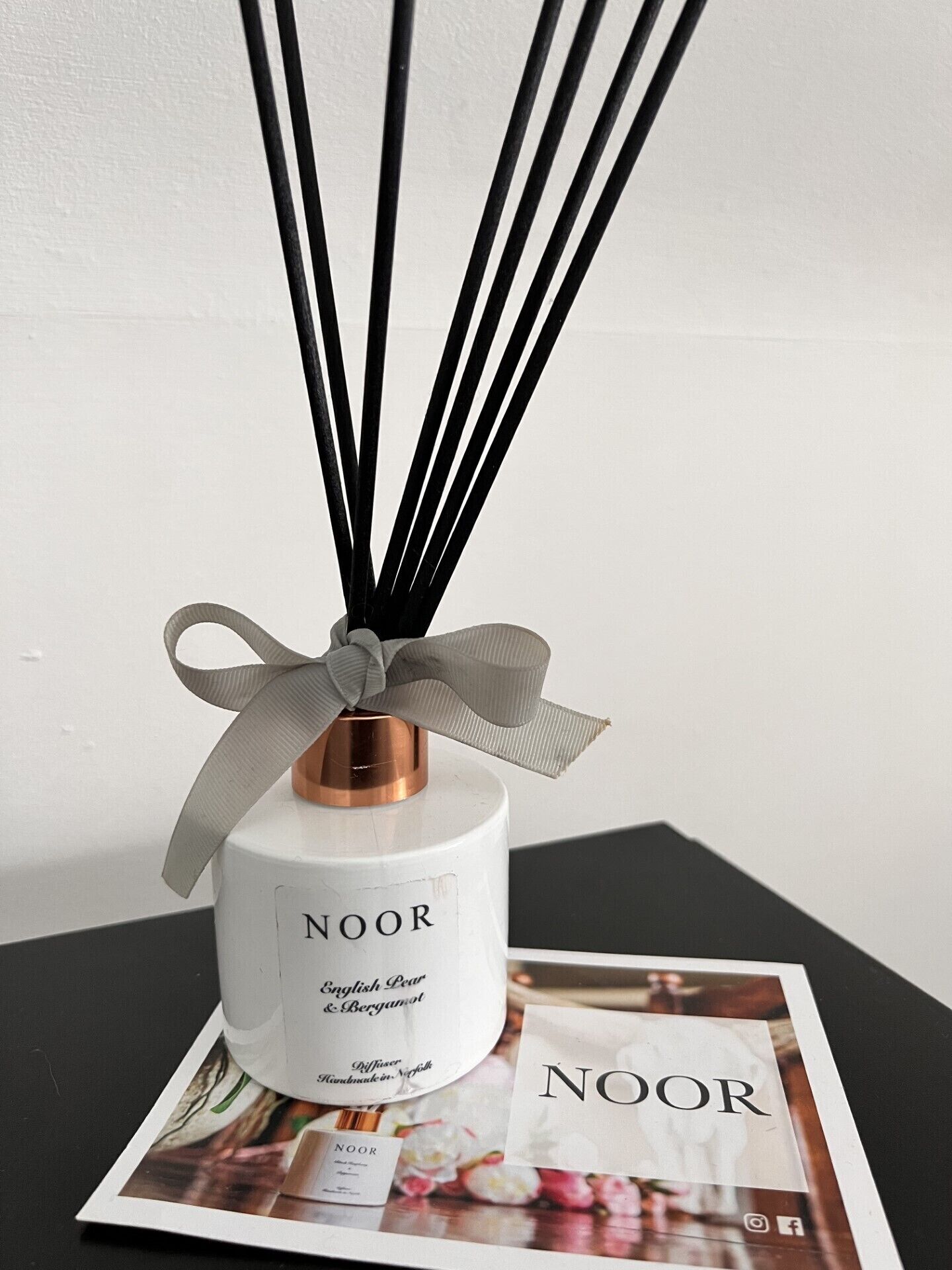 Een NOOR English Pear & Bergamot sinaasappelstrooier met lint, geplaatst op een tafel met een NOOR tijdschrift.