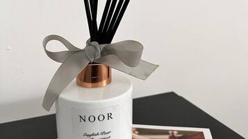 A NOOR English Pear & Bergamot reed diffuser with a ribbon, placed on a table with a NOOR magazine.