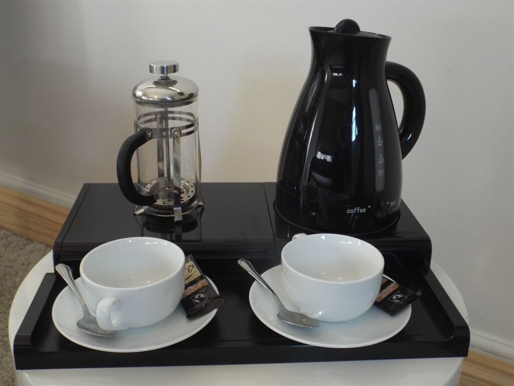 A coffee station with a French press and a coffee maker, two white cups with saucers, and a tray.