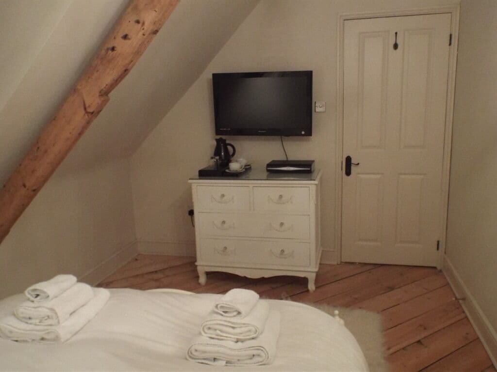 Une chambre à coucher avec un lit, une commode blanche, un téléviseur à écran plat et une porte.