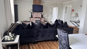 Een moderne woonkamer met een zwarte bank, een open haard en een flatscreen televisie.